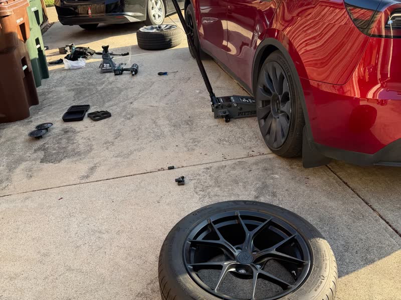 Tesla Model Y raised on an EV-rated floor jack while the damaged Michelin 235/55 ZR18 wheel sits on the driveway during a mobile tire change in Dallas–Fort Worth